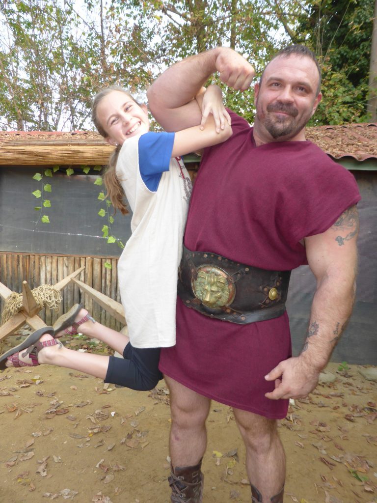 Gladiator School Rome Girls hangs from gladiator's huge bicep